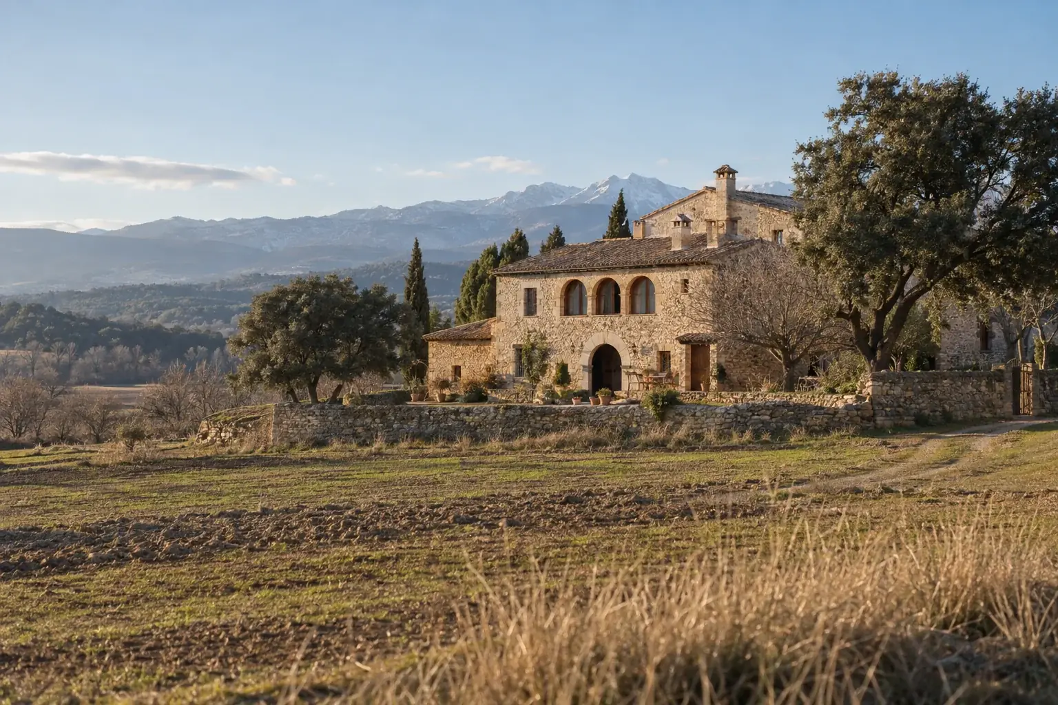 Masía catalana de piedra en pleno campo, con montañas al fondo